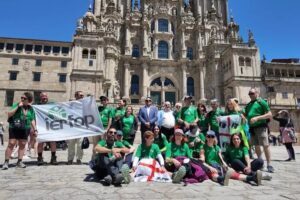 Gruppo di partecipanti al Cammino di Santiago di Compostela dvanti alla Cattedrale con bandiera Ierfop e bandiere sarde.